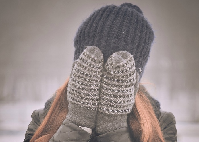 Woman covering her face with gloved hands