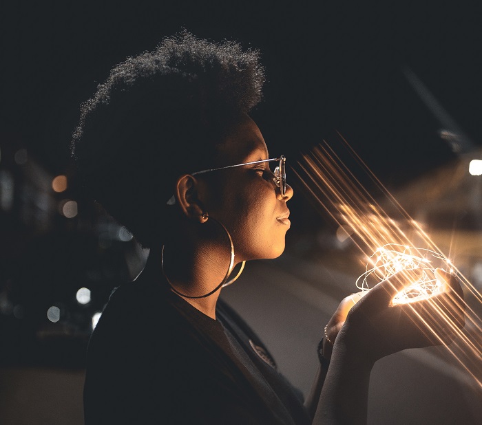 A young woman stands outdoors at night holding a handful of fairy lights