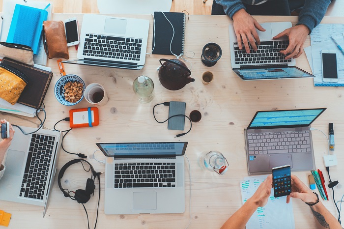 People work on a breakfast table crowded with laptops, phones, paper and pens