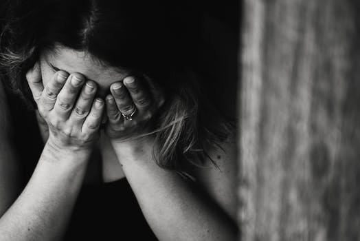 A black and white images of female with head in her hands looking troubled. 