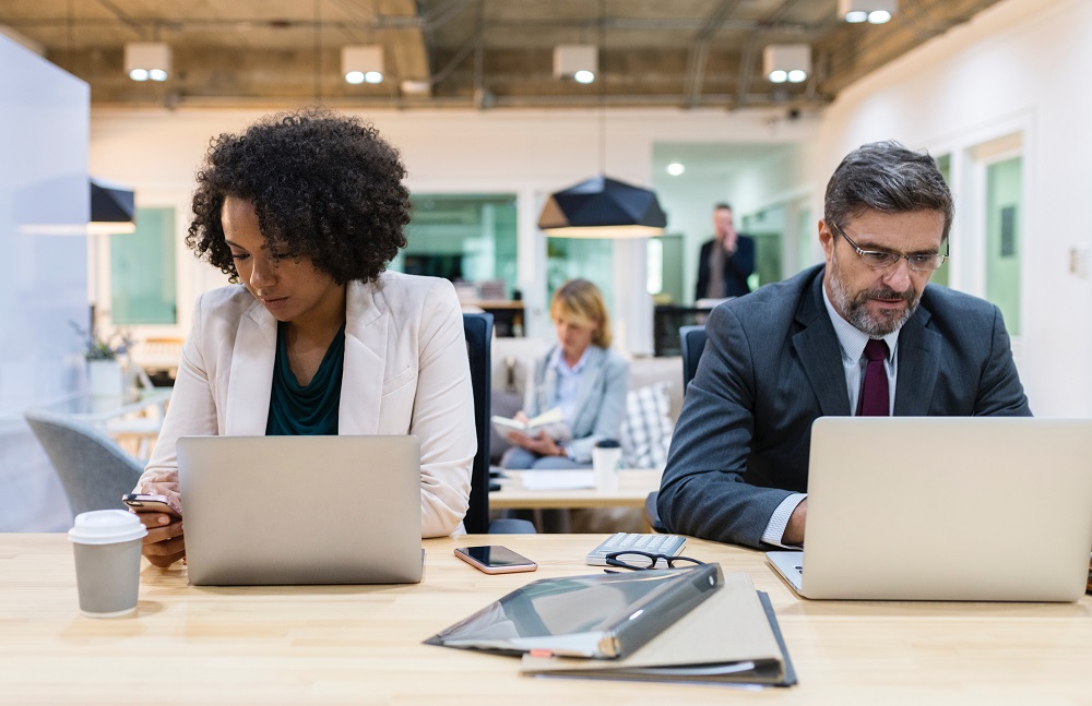 An Afro-Caribbean woman and a white man sit side-by-side working on laptops