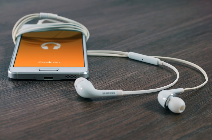 A smartphone with earbuds displays Google Play music streaming