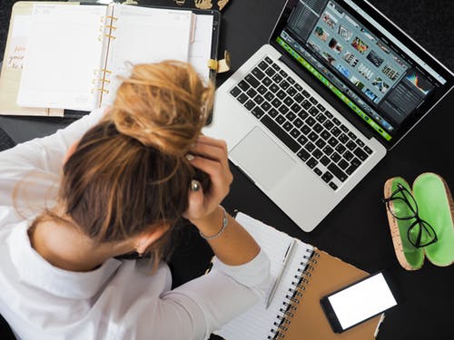 Female working in front of a laptop surrounded by papers - her head cupped in her hands.