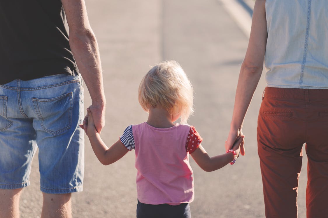 Two parents holding hands with their daughter from the rear view.